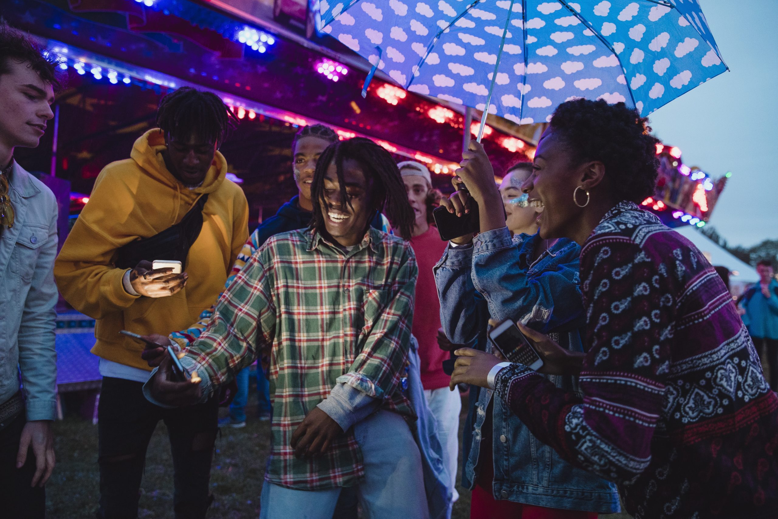 Small group of young adults are videoing themselves dancing in the rain while at a funfair.