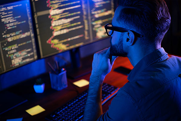 A computer software developer writing and reviewing his code in a dark office.